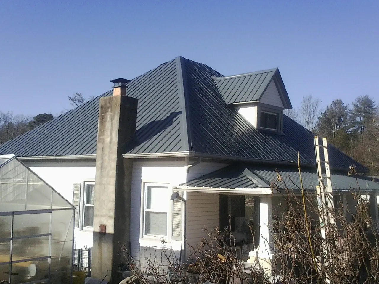 Dark blue standing seam metal roof on a white farmhouse with dormer — Slate & Tile Roof Repair by Roofing Brothers in Pleasant Valley