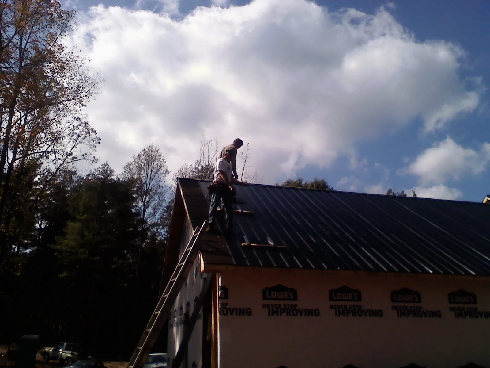 Roofer fastening dark metal panels high against a cloudy sky, from a Roof Inspection job in Pleasant Valley
