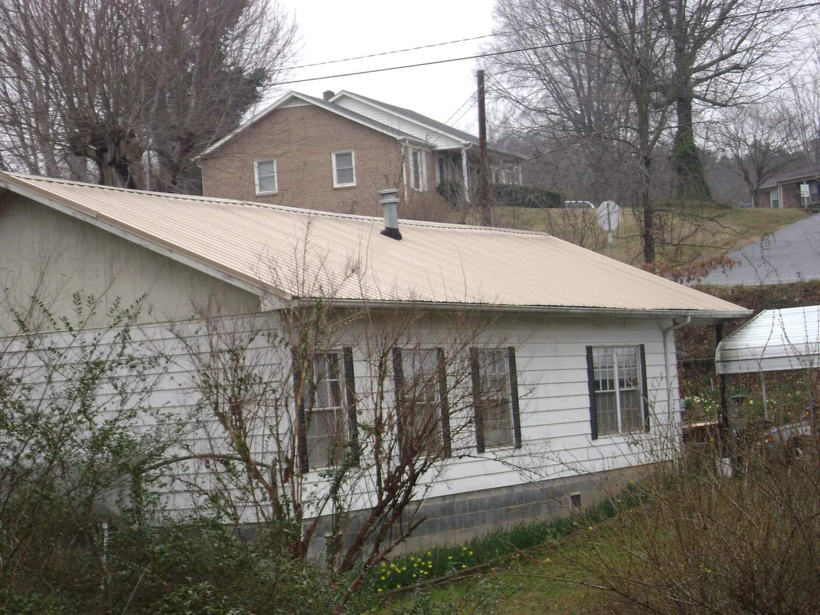 Tan metal roof on a white sided house set into a hillside — Commercial Roofing by Roofing Brothers in Pleasant Valley